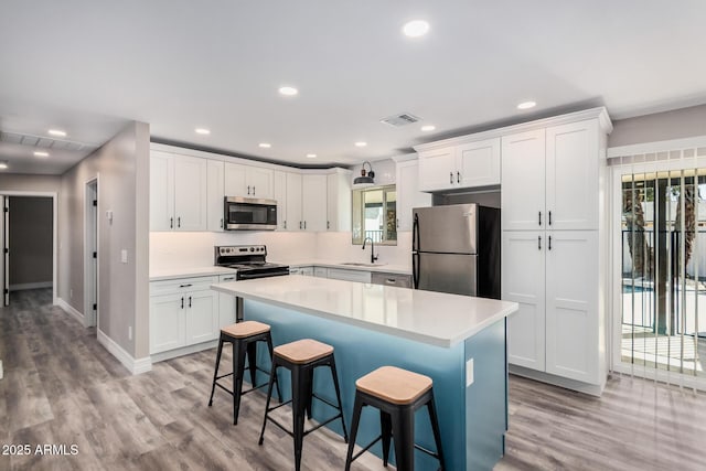 kitchen with visible vents, a sink, a kitchen breakfast bar, appliances with stainless steel finishes, and white cabinets