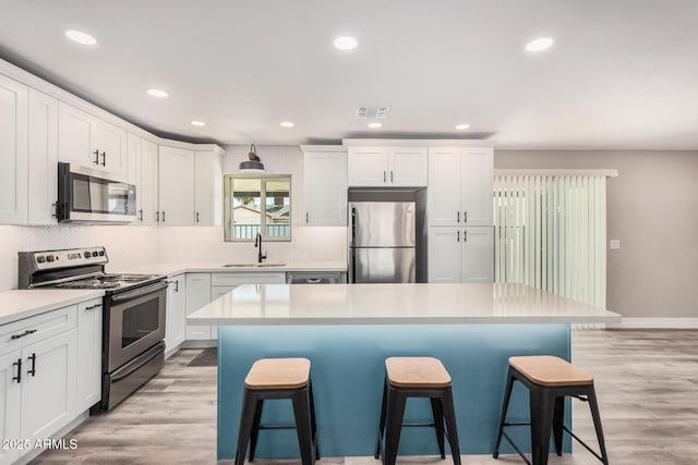 kitchen with visible vents, a sink, appliances with stainless steel finishes, white cabinetry, and a kitchen breakfast bar