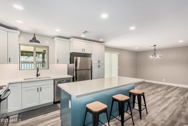 kitchen featuring light wood finished floors, visible vents, a kitchen bar, appliances with stainless steel finishes, and a sink