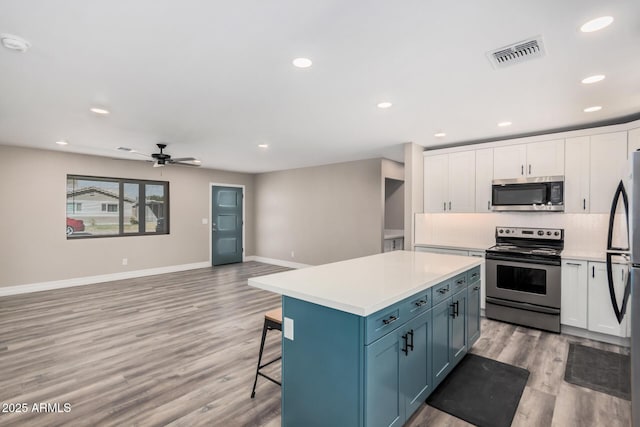 kitchen with visible vents, backsplash, appliances with stainless steel finishes, a breakfast bar area, and white cabinets