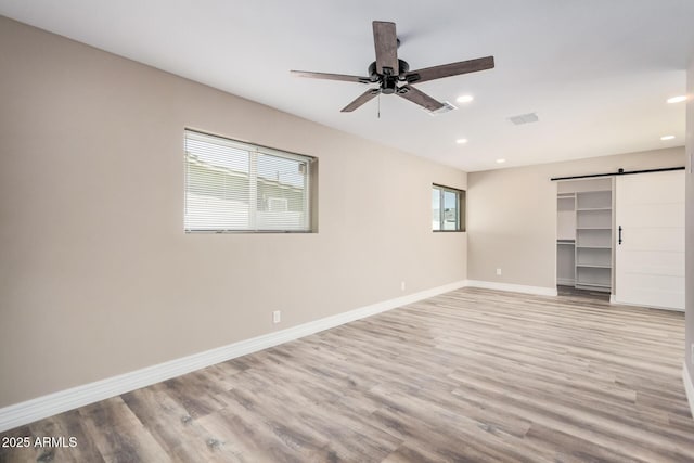 unfurnished bedroom with baseboards, visible vents, light wood finished floors, recessed lighting, and a barn door