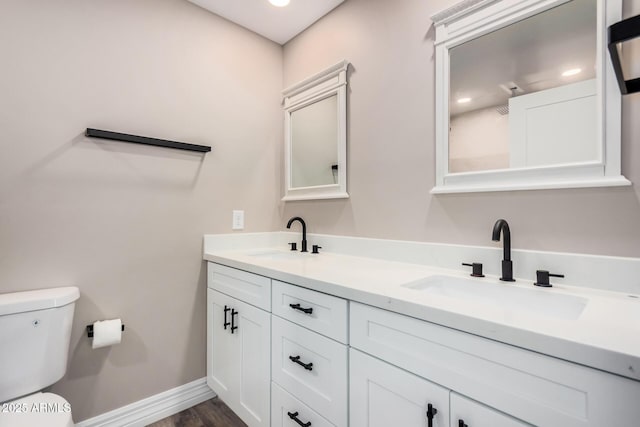 bathroom featuring double vanity, toilet, baseboards, and a sink