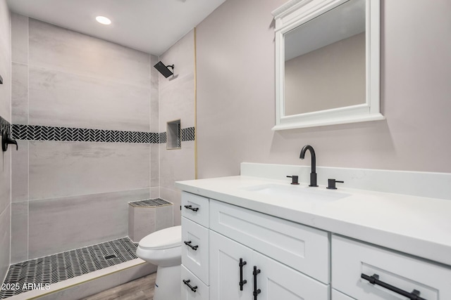 bathroom featuring toilet, recessed lighting, tiled shower, wood finished floors, and vanity