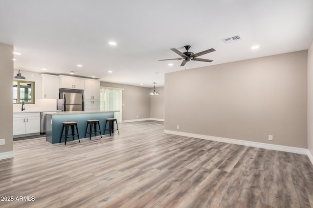 kitchen with visible vents, a kitchen bar, freestanding refrigerator, light wood-style floors, and white cabinets