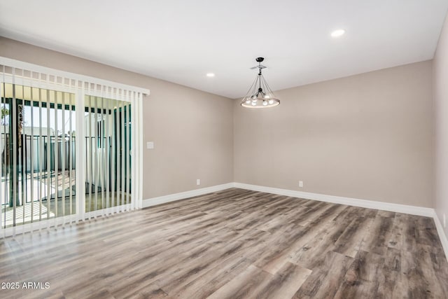 spare room featuring a chandelier, recessed lighting, baseboards, and wood finished floors