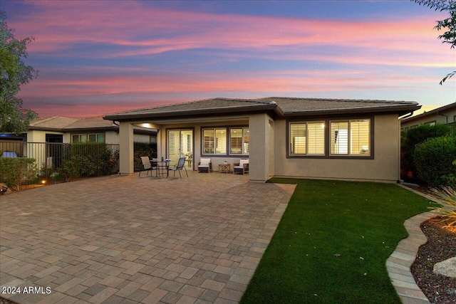 back house at dusk with a patio and a yard