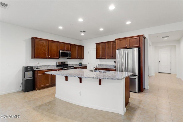 kitchen with a kitchen breakfast bar, light stone countertops, stainless steel appliances, a center island with sink, and sink