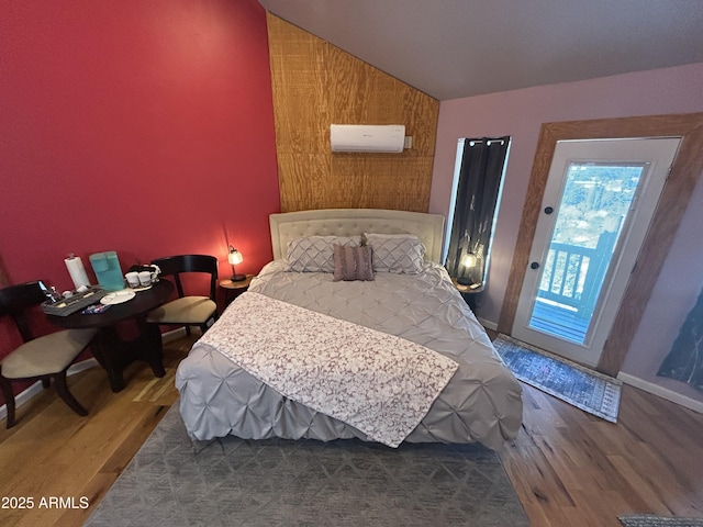 bedroom featuring a wall unit AC, baseboards, vaulted ceiling, and wood finished floors