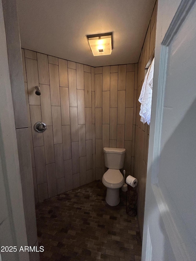 bathroom featuring toilet, brick floor, and a tile shower