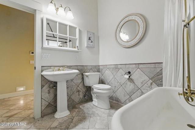 full bath featuring a soaking tub, wainscoting, a sink, and toilet