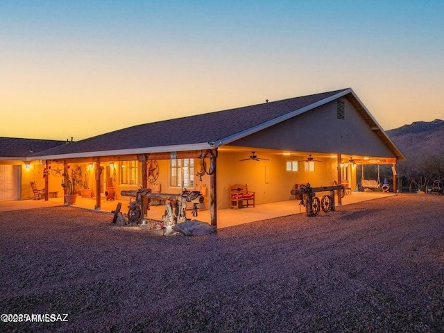 back of house at dusk featuring stucco siding, a ceiling fan, and a patio