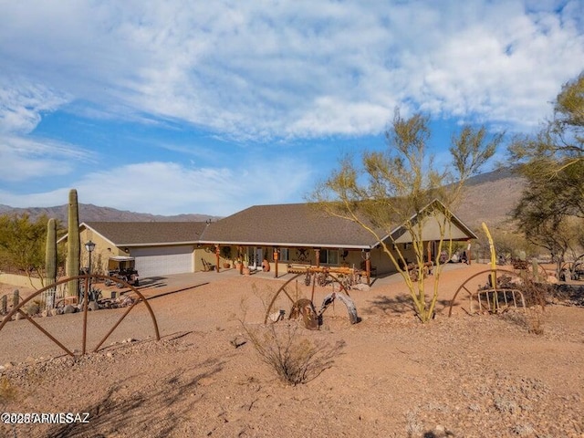 view of front of house with dirt driveway, stucco siding, an attached garage, a porch, and a mountain view