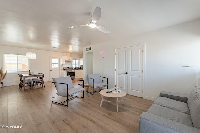 living room featuring a ceiling fan, visible vents, light wood-style flooring, and baseboards