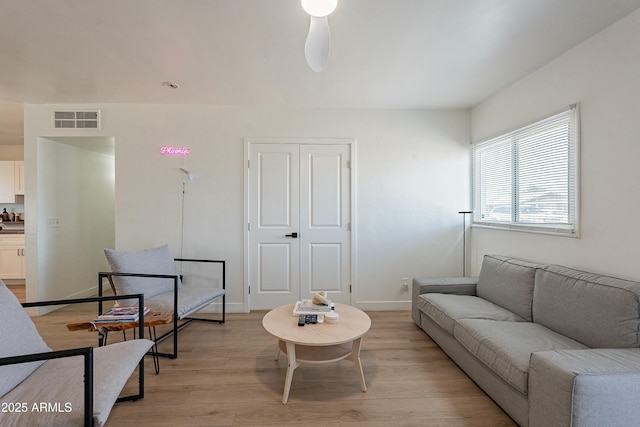 living room featuring a ceiling fan, light wood-style flooring, visible vents, and baseboards