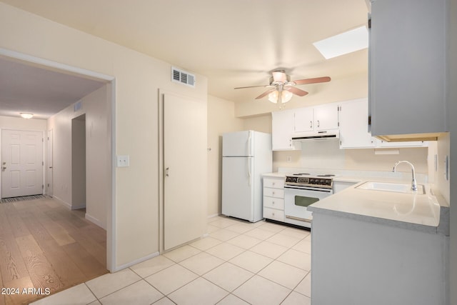 kitchen featuring white appliances, white cabinetry, a skylight, sink, and light tile patterned flooring