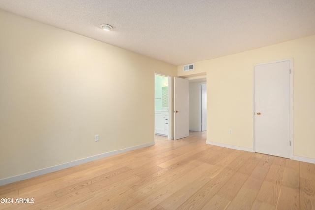 empty room with light wood-type flooring and a textured ceiling