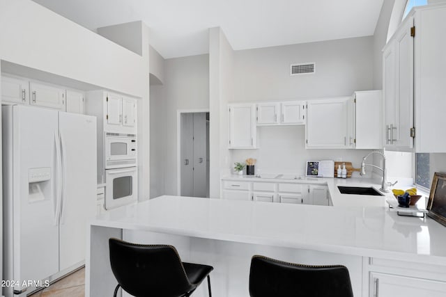 kitchen featuring kitchen peninsula, a kitchen breakfast bar, white appliances, sink, and white cabinets