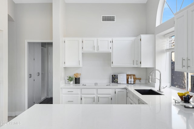 kitchen with cooktop, white cabinetry, sink, and a towering ceiling