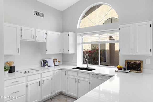 kitchen featuring dishwasher, white cabinets, sink, light tile patterned floors, and a towering ceiling