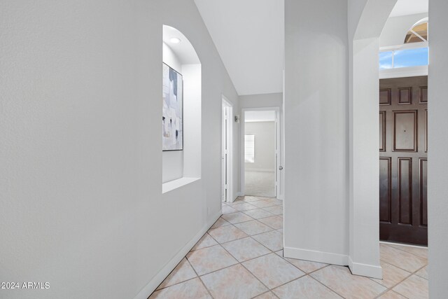 hall with light tile patterned floors, a wealth of natural light, and vaulted ceiling