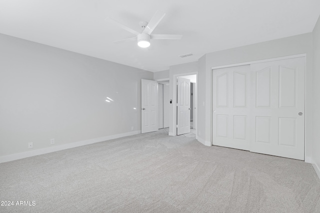 unfurnished bedroom featuring ceiling fan, light colored carpet, and a closet