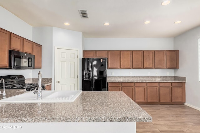 20261 W Desert Bloom St, Buckeye, AZ 85326 - kitchen featuring brown cabinetry, recessed lighting, light wood-style floors, and black appliances