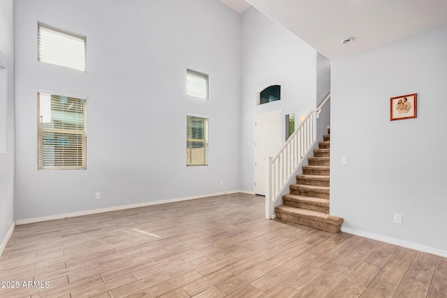 20261 W Desert Bloom St, Buckeye, AZ 85326 - unfurnished living room with stairs, baseboards, light wood-style flooring, and a high ceiling