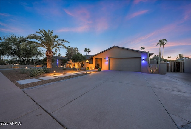 view of front facade with driveway, a garage, fence, stucco siding, and a gate
