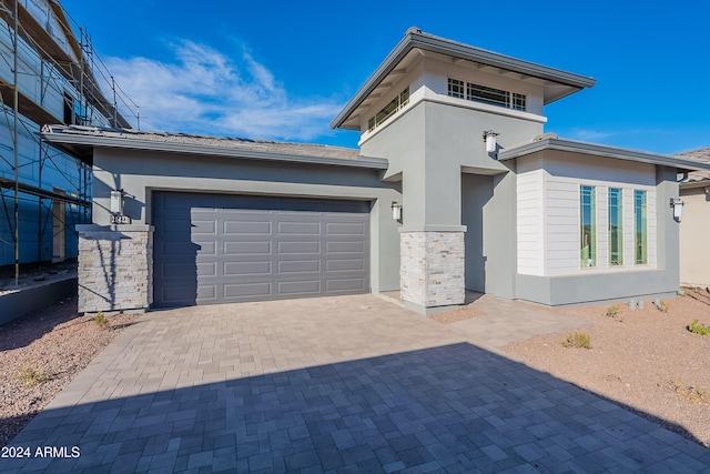 prairie-style house featuring a garage, decorative driveway, stone siding, and stucco siding