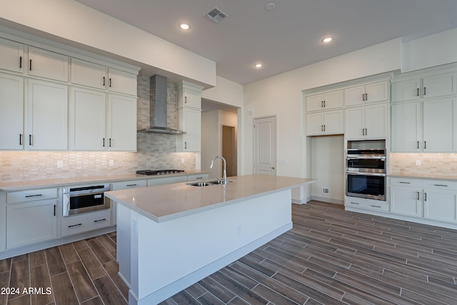 kitchen with wood finish floors, stainless steel appliances, a sink, light countertops, and wall chimney exhaust hood