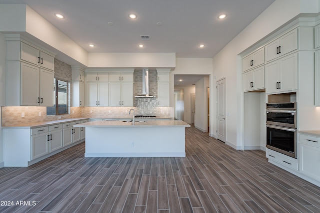 kitchen with visible vents, double oven, wall chimney exhaust hood, and wood tiled floor