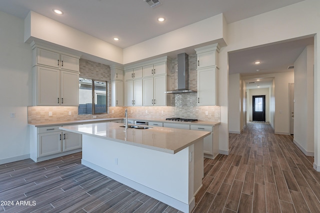 kitchen with a sink, wall chimney exhaust hood, light countertops, wood tiled floor, and stainless steel gas cooktop