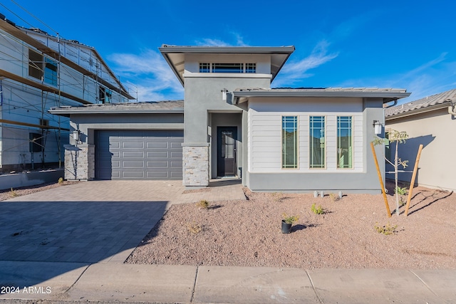 prairie-style house featuring stone siding, stucco siding, an attached garage, and decorative driveway