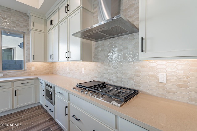 kitchen with backsplash, stainless steel appliances, wall chimney exhaust hood, white cabinets, and light countertops