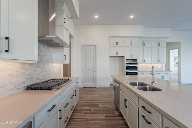 kitchen featuring wood finish floors, a sink, stainless steel appliances, wall chimney exhaust hood, and white cabinets