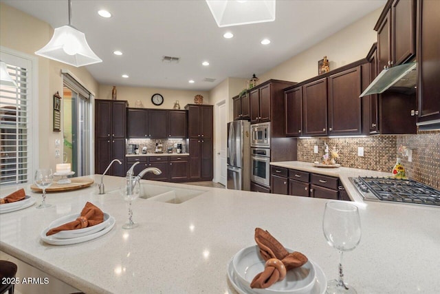 kitchen with decorative backsplash, kitchen peninsula, stainless steel appliances, sink, and decorative light fixtures