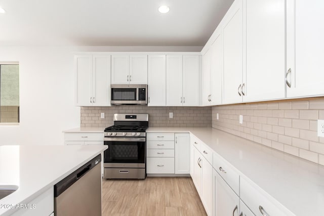 kitchen with appliances with stainless steel finishes, light wood-type flooring, white cabinets, and decorative backsplash