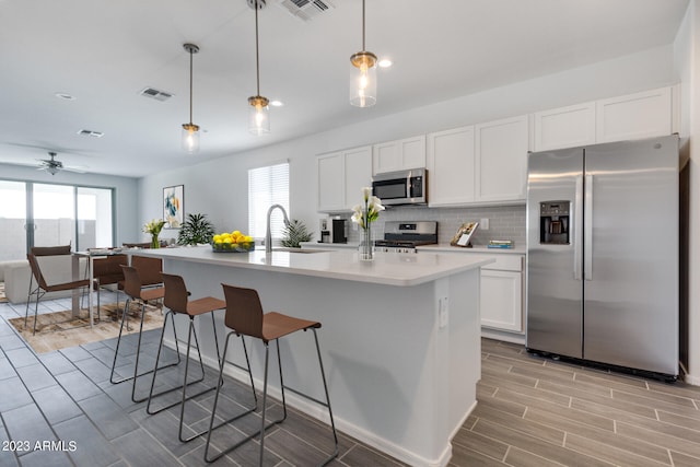 kitchen featuring appliances with stainless steel finishes, tasteful backsplash, an island with sink, ceiling fan, and decorative light fixtures