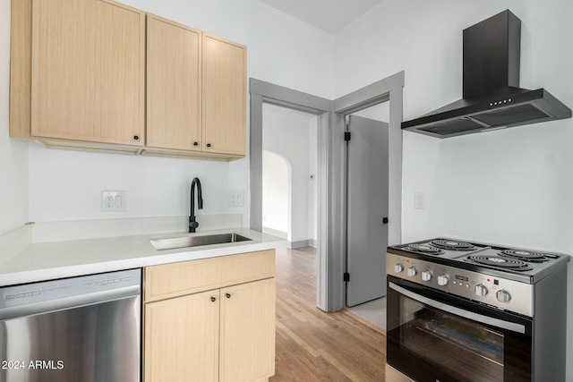 kitchen with sink, wall chimney exhaust hood, light brown cabinets, light hardwood / wood-style floors, and appliances with stainless steel finishes