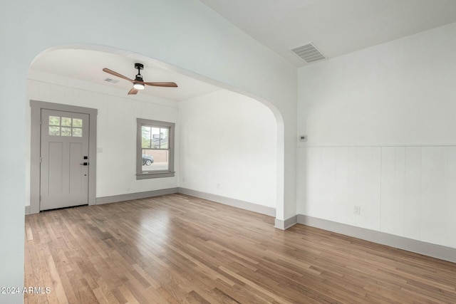 foyer featuring ceiling fan, light wood-type flooring, and wooden walls