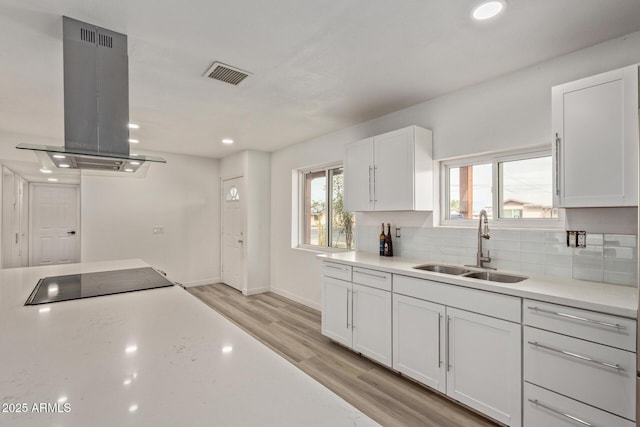 kitchen featuring sink, white cabinets, decorative backsplash, island exhaust hood, and light hardwood / wood-style floors