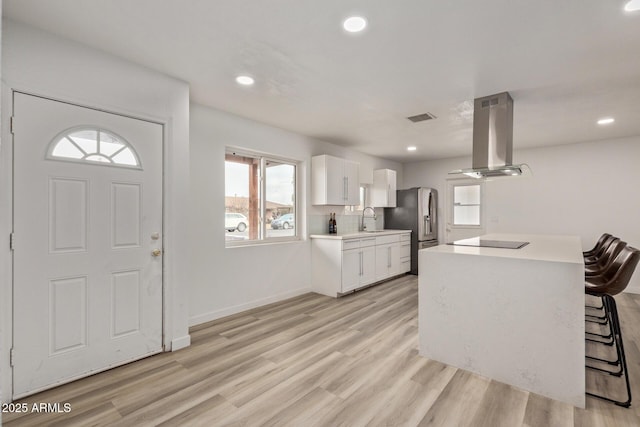 kitchen featuring a breakfast bar, island range hood, white cabinets, stainless steel refrigerator with ice dispenser, and light hardwood / wood-style flooring