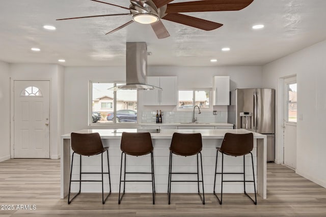 kitchen featuring sink, stainless steel fridge, a breakfast bar, white cabinetry, and island range hood