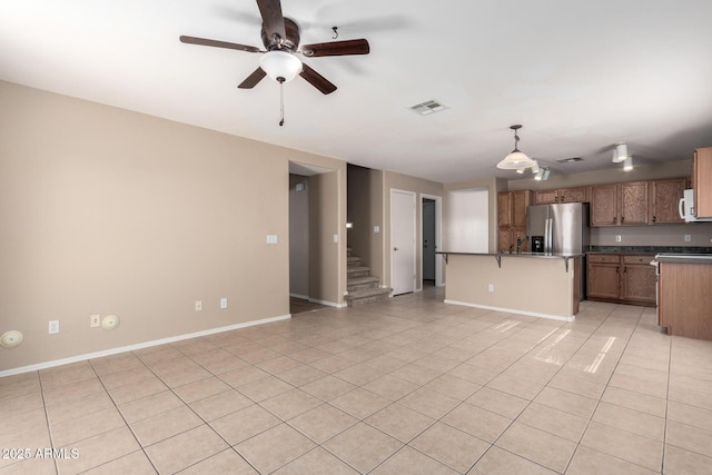 kitchen featuring white microwave, light tile patterned flooring, visible vents, dark countertops, and stainless steel fridge