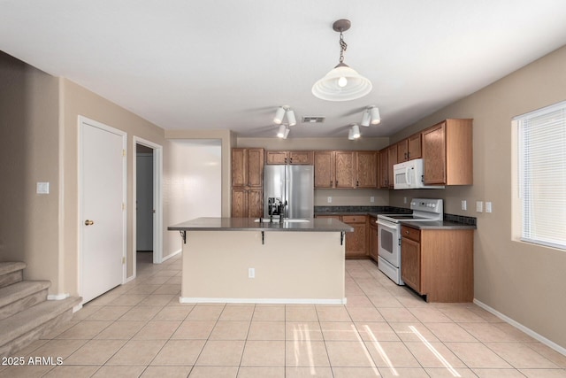 kitchen with light tile patterned flooring, white appliances, hanging light fixtures, brown cabinets, and dark countertops