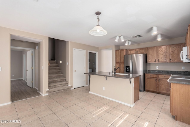 kitchen featuring light tile patterned floors, visible vents, dark countertops, brown cabinets, and stainless steel refrigerator with ice dispenser