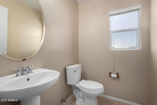 half bath featuring a sink, tile patterned flooring, toilet, and baseboards