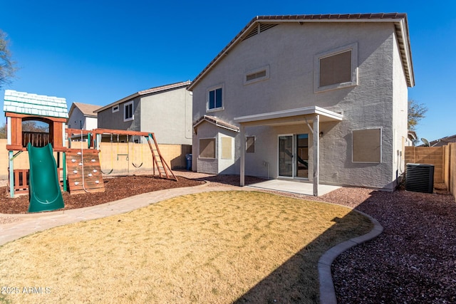 rear view of house with cooling unit, fence, a playground, and stucco siding