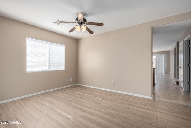 spare room featuring a ceiling fan, light wood-type flooring, a wealth of natural light, and baseboards