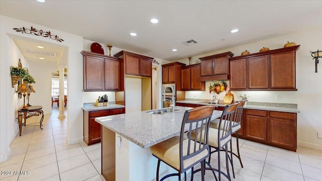 kitchen with light stone countertops, light tile patterned floors, a center island with sink, and built in microwave